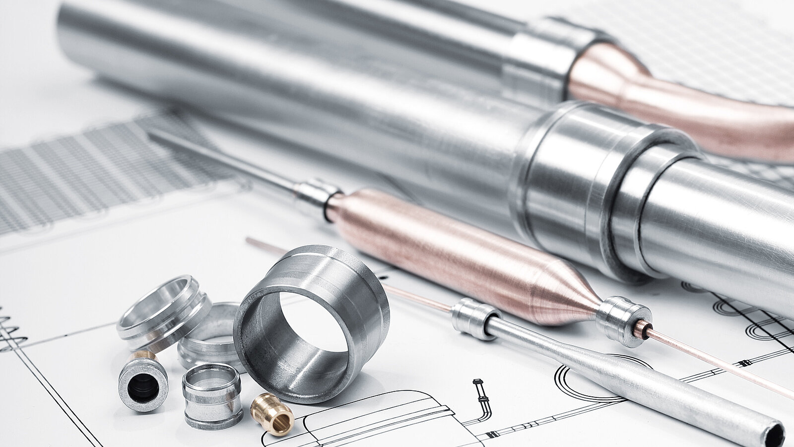 Mehrere metallische Zylinder, Rohre und Fittings auf technischen Zeichnungen mit Linien, Maßen und Anmerkungen; daneben ein Stift und ein Lineal.