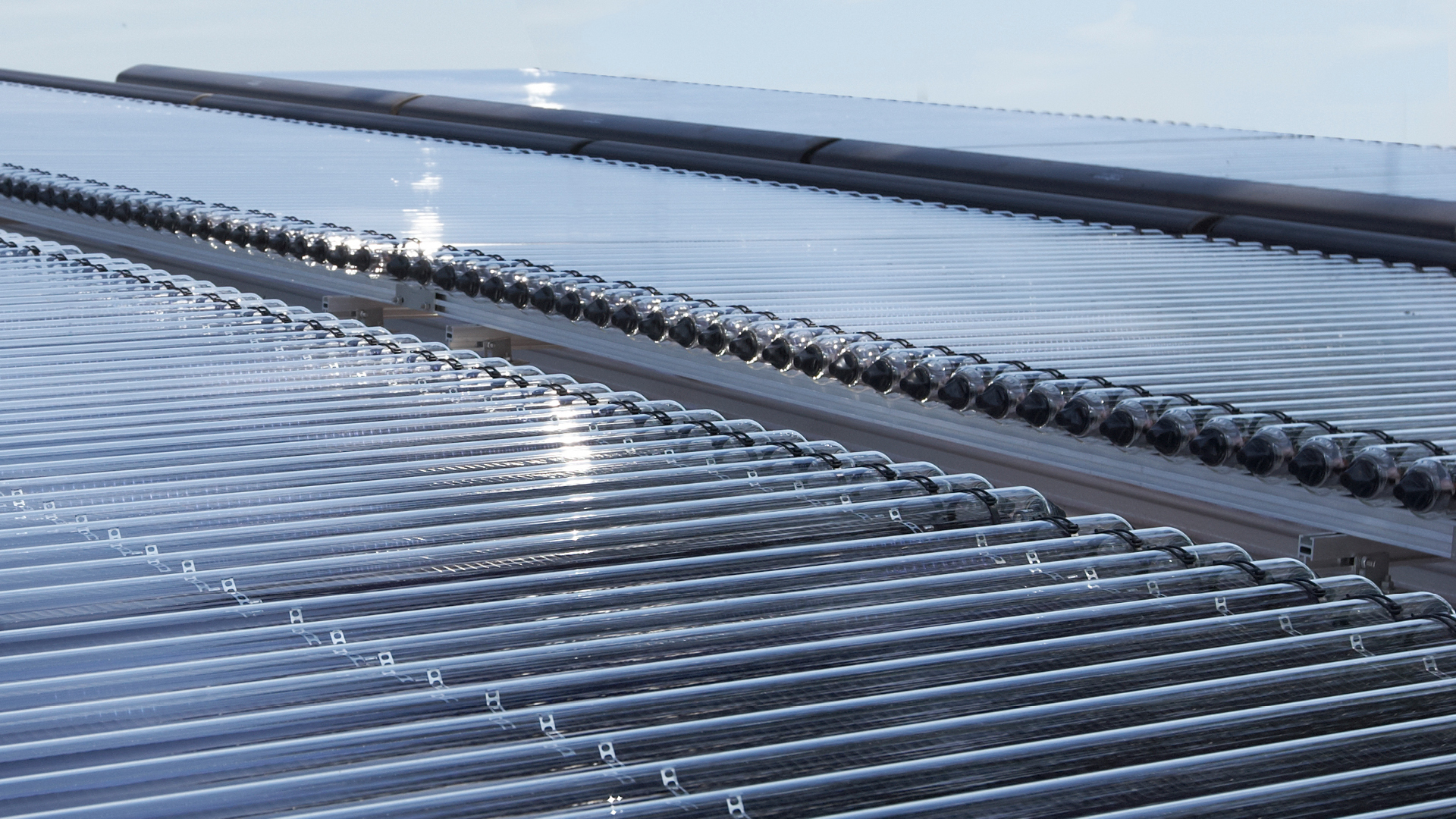 Primer plano de paneles solares con reflejos de luz solar en la superficie, dispuestos en filas con patrones de luz y sombra.