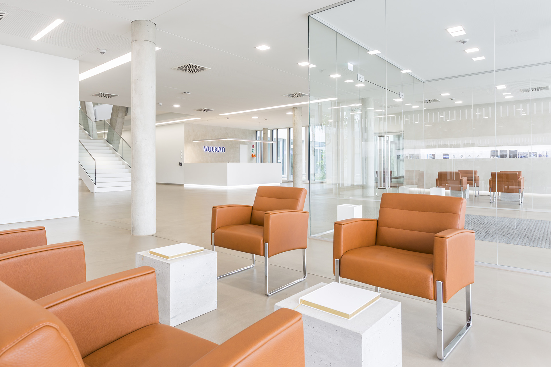 The lobby of the administration building. In the foreground, four brown armchairs face each other. Between them are small tables.